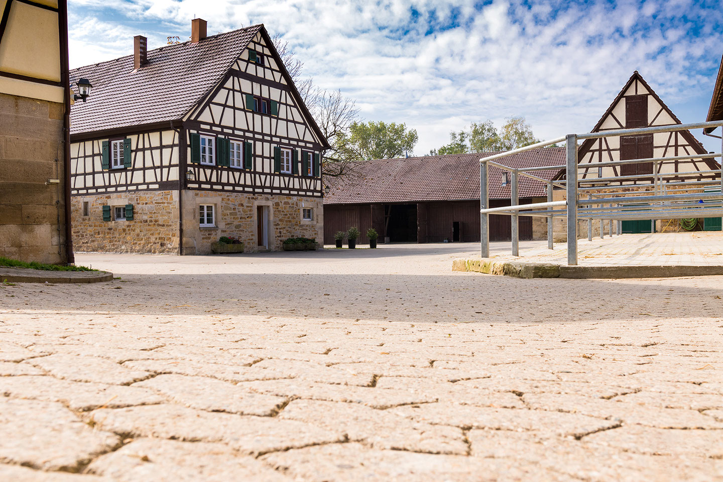 Gepflasterter Hof mit Fachwerkhaus, grünen Fensterläden und Paddockauslauf
