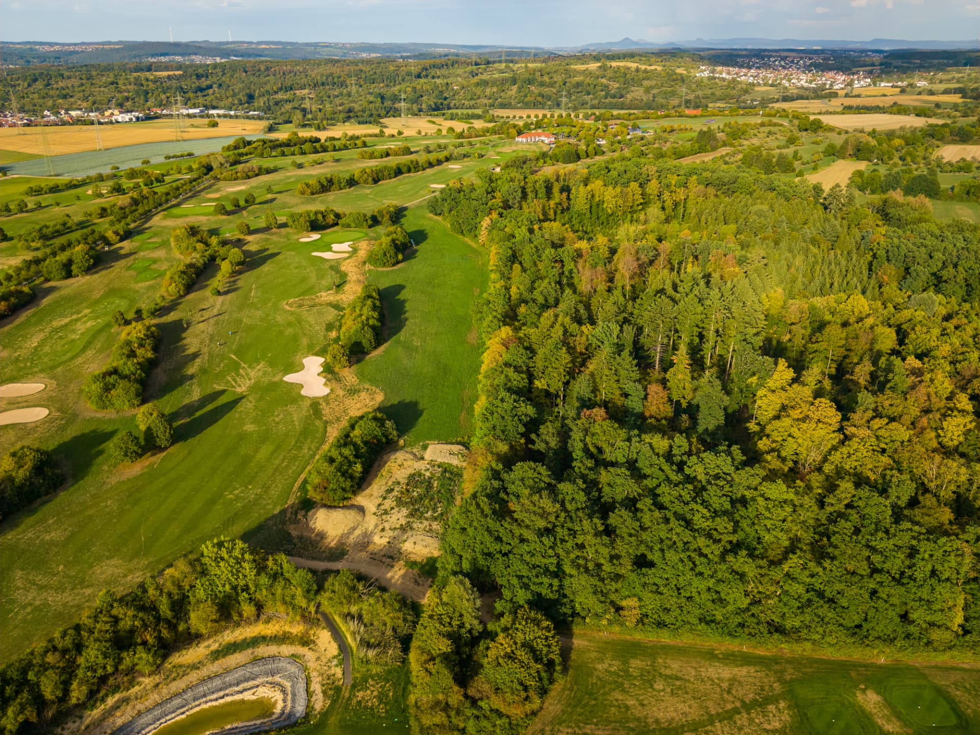 Drohnenaufnahme des Golfplatzes zwischen Wald, Wasserbassin und Äckern