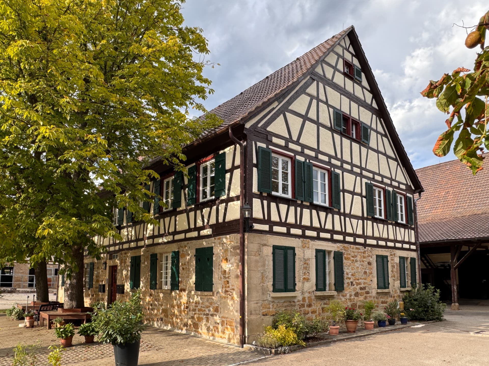 Fachwerk-Verwalterhaus des Hofguts mit grünen Fensterläden und Kastanienbaum