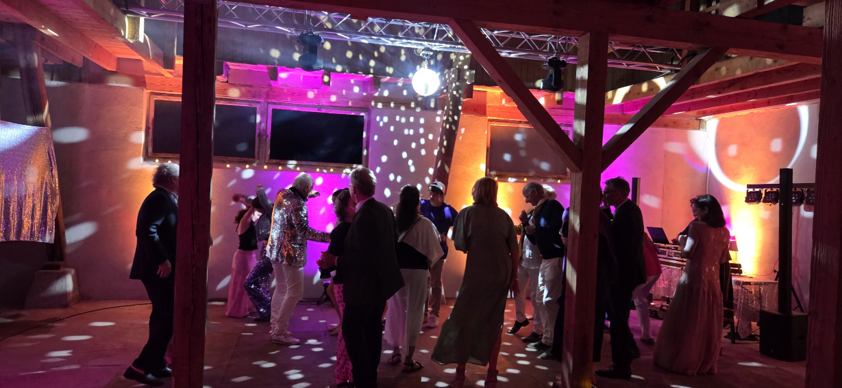 Abendliche Feier in der ausgebauten Scheune mit tanzenden Gästen, Discokugel, farbiger Lichtshow und DJ-Pult