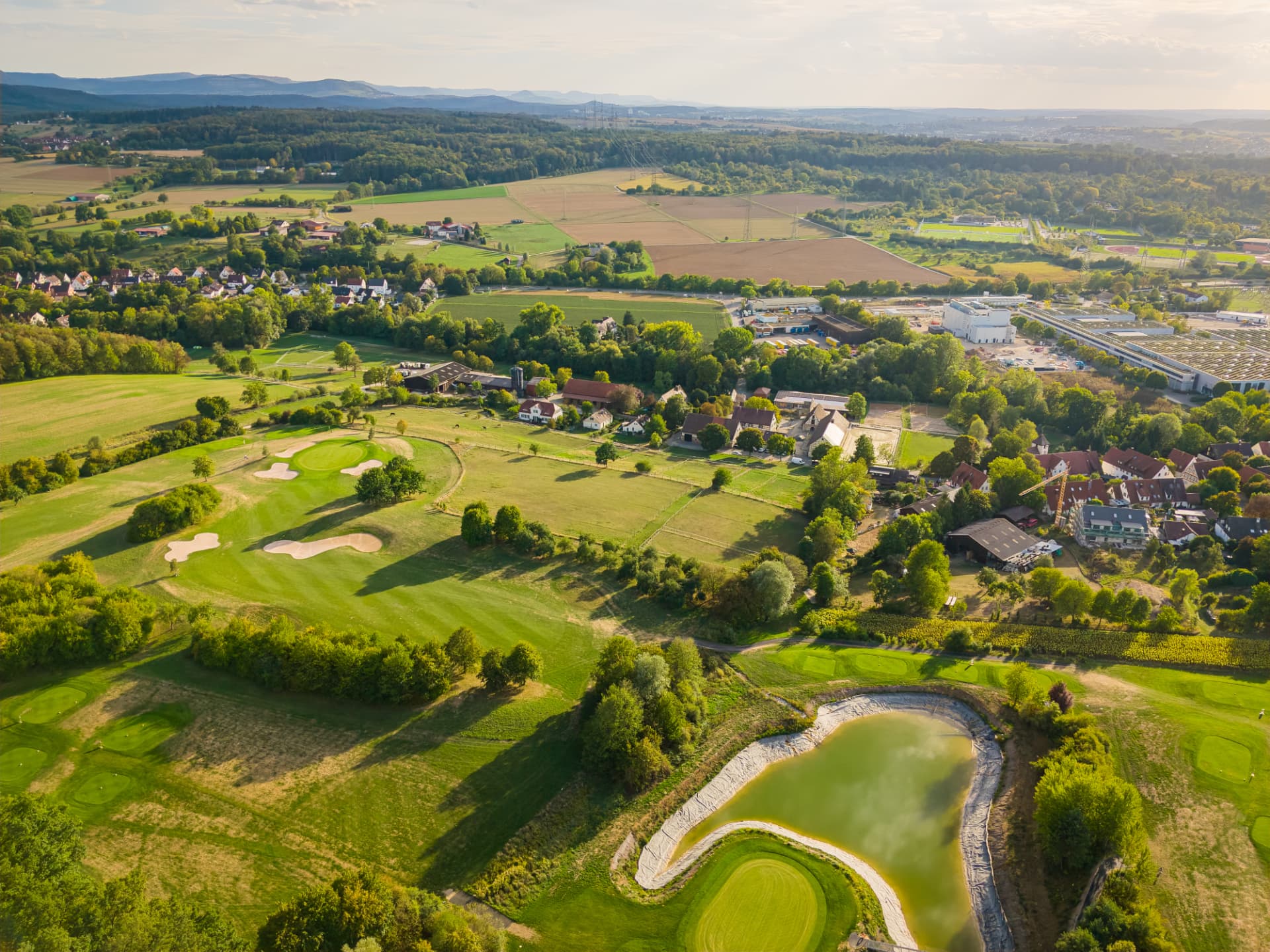 Luftbild vom Golfplatz mit Wasserhindernis auf das Dorf